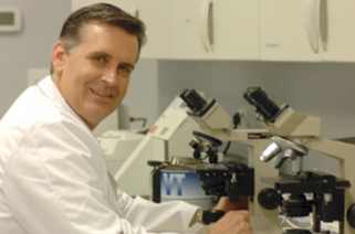 Dr. Baker sitting in the lab at a microscope smiling at camera